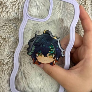 May include: A clear phone case with a wavy lavender border and a central circular accessory featuring a stylized anime character head with dark blue hair, green eyes, and a green patterned headband, designed for a mobile device.