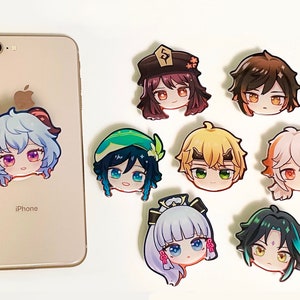 May include: A collection of eight colorful anime-style character head stickers. One sticker is attached to the back of a light-colored iPhone, while the other seven are arranged to the right, featuring various hair colors and facial expressions.