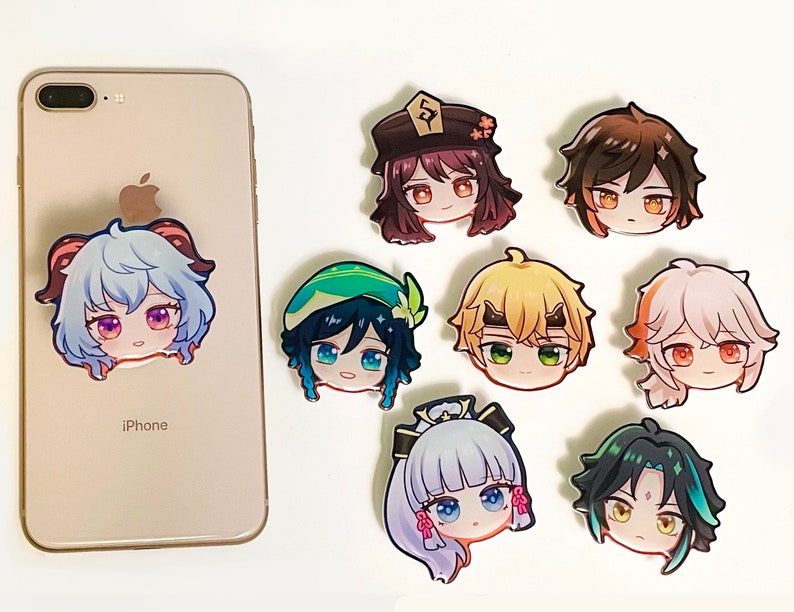 May include: A collection of eight colorful anime-style character head stickers. One sticker is attached to the back of a light-colored iPhone, while the other seven are arranged to the right, featuring various hair colors and facial expressions.