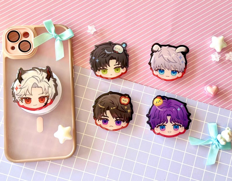 May include: A clear phone case with a pop socket featuring a cartoon character with white hair and red eyes. Four additional cartoon character face stickers are displayed on a pink and white striped surface.