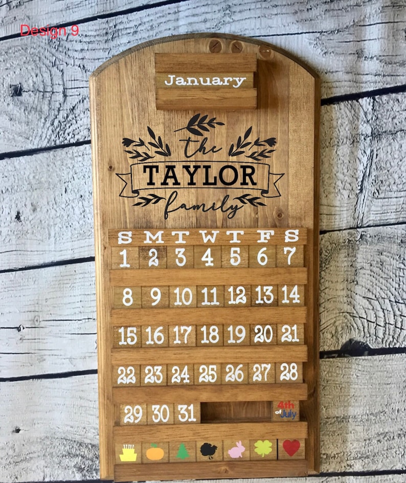 May include: A wooden calendar with the text "January" and "the TAYLOR family" on it. The calendar has a slot for each day of the month and a small slot for a note. The calendar is decorated with small wooden blocks with numbers on them. The calendar is also decorated with small wooden blocks with different designs on them, including a pumpkin, a Christmas tree, a turkey, a bunny, a shamrock, and a heart.