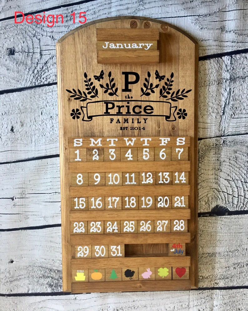 May include: A wooden calendar with a white background and black lettering. The calendar is decorated with a floral design and the text "P the Price Family Est 2014". The calendar has a slot for each day of the month and a small slot for the month name. The calendar is decorated with a small American flag and the text "4th of July".