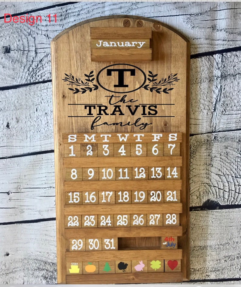 May include: A wooden calendar with the word "January" at the top. The calendar is decorated with a wreath of leaves and the text "the TRAVIS family". The calendar has a letter "T" in a circle at the top. The calendar has a slot for each day of the month and a small slot at the bottom for a special occasion.