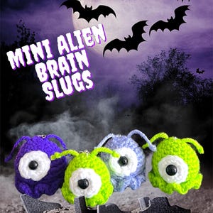 May include: Three crocheted alien brain slugs in purple, green, and blue with white eyes. The slugs are against a dark background with a full moon and bats.