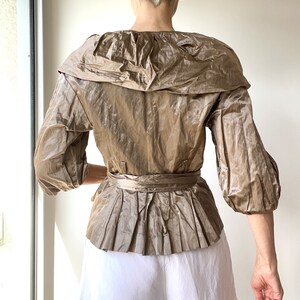 Pode incluir: Top bege de manga curta com gola larga e peplum plissado. O top apresenta um cinto a condizer e &eacute; feito de um tecido brilhante e texturizado. A modelo usa cal&ccedil;&otilde;es brancos.