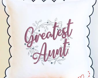 May include: White square pillow with a scalloped edge and a dark navy blue trim. The pillow features the embroidered text "Greatest Aunt" in a cursive font, surrounded by a floral wreath. The text "THE EMBROIDERY DESIGN SPOT" is at the bottom.