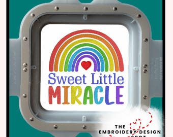 May include: A white square with a rainbow design and the words "Sweet Little Miracle" in colorful embroidery. The design is set within a silver embroidery hoop, perfect for crafting projects. The Embroidery Design Spot logo is in the bottom right corner.