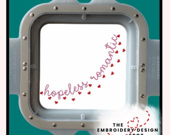 May include: A square embroidery hoop with the words "hopeless romantic" in pink script, accented with small red hearts. The text is inside the hoop, which is surrounded by a silver frame. The Embroidery Design Spot logo is at the bottom.