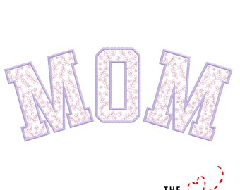 May include: The word "MOM" in a stylized font, with each letter outlined in lavender and filled with a floral pattern. The design is set against a white background, with the text "THE EMBROIDERY DESIGN SPOT" at the bottom.