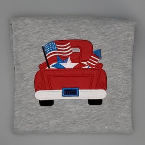 May include: Red pickup truck with a white license plate that says "7704". The truck bed is filled with American flags and stars.
