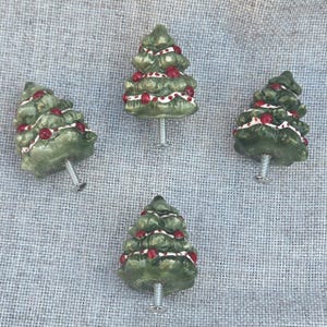 May include: Four green ceramic Christmas tree drawer pulls with red and white accents. Each pull has a silver screw.