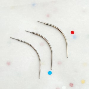 May include: Three silver-toned curved metal needles with a smooth, polished finish. Each needle features a straight, thin post at one end that transitions into a gentle arc, designed for specialized sewing or craft applications.