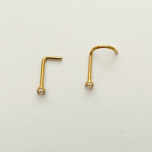 Può includere: Due anelli per il naso in oro con una piccola pietra preziosa trasparente all'estremità di ogni anello.