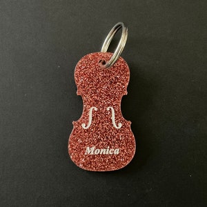 May include: A pink glitter violin keychain with the name "Monica" engraved on it.