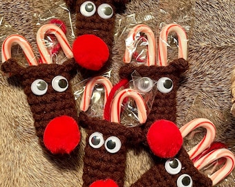 May include: A collection of handmade Christmas ornaments shaped like reindeer. Each ornament is brown with googly eyes, a red pom-pom nose, and candy cane antlers. The ornaments are packaged in clear plastic.
