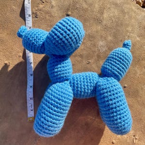May include: A blue crocheted balloon animal shaped like a dog. The dog is lying on a brown, textured surface.