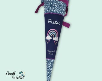 May include: A dark blue fabric cone with a top section featuring a white speckled pattern and a purple ribbon tie. The center displays the name Elisa, a rainbow graphic with clouds and hearts, and the text August 2023 in white lettering.