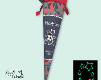 May include: A cone-shaped school gift bag featuring a dark grey and red geometric pattern at the top with a red ribbon tie. The lower section is dark grey with the name Matteo, a football graphic, and the text August 2023 in white.