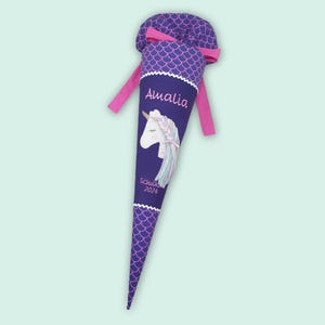 Könnte beinhalten: Eine lila-rosa Schultüte mit einem Einhorn-Design. Die Tüte trägt den Namen "Amalia" und das Jahr "2024". Die Tüte hat einen gewellten Rand und ein rosa Band.