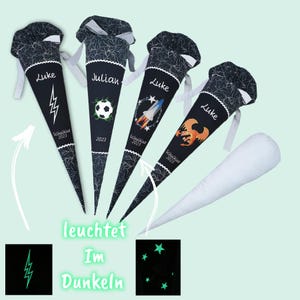 Könnte beinhalten: Vier schwarz-weiße Schultüten mit personalisierten Namen und Designs, darunter ein Blitz, ein Fußball, eine Rakete und ein Drache. Auf jeder Tüte ist das Jahr 2023 aufgedruckt. Der Text "leuchtet Im Dunkeln" ist ebenfalls sichtbar.