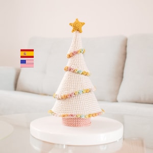 Può includere: Un albero di Natale bianco all'uncinetto con una base rosa e una stella gialla in cima. L'albero è decorato con fiori all'uncinetto colorati.