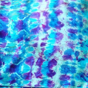 May include: A tie-dye fabric with a blue and purple color scheme. The fabric has a mottled appearance with shades of blue, purple, and white.