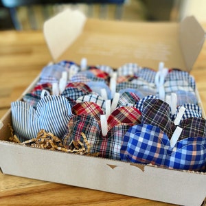 May include: A box filled with handmade heart-shaped pillows. The pillows are made from various plaid fabrics in blue, red, and white.