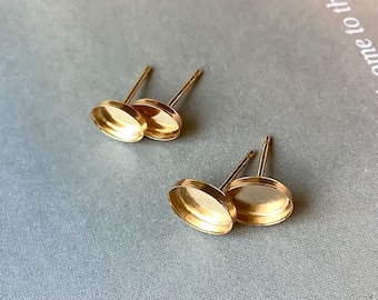 May include: Four gold-colored oval earring posts with a shallow dish design. The posts are thin and straight, and the earring backs are not visible. The earrings are set against a light blue-gray background.