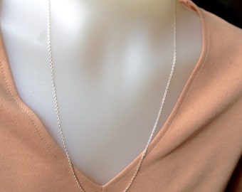 May include: A delicate silver necklace with a fine chain is displayed against a peach-colored top. The necklace is draped around a mannequin's neck, showcasing its length and design. The chain appears to be approximately 24 inches long.