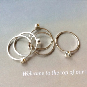 May include: A collection of silver-colored rings with small, square-shaped accents. The rings are arranged on a light gray surface, with the text "Welcome to the top of our" visible in the bottom portion of the image.