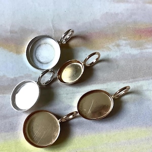 May include: A selection of jewellery findings, including silver and gold-toned oval and round bezel pendant trays with loop bails. These components are for crafting custom jewellery.
