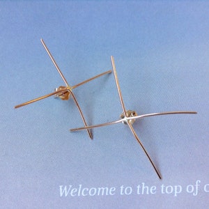 May include: Two pairs of gold-colored metal earring components, each with four straight arms extending from a central post. The earrings are displayed on a light blue surface with the text "Welcome to the top of" at the bottom.
