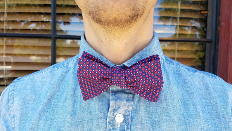 May include: A blue denim shirt with a red and white bow tie featuring a star pattern.