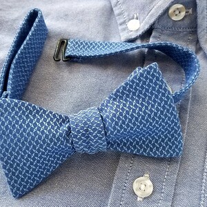 May include: A blue bow tie with a geometric pattern. The bow tie is made of a soft, textured fabric and has a classic design.