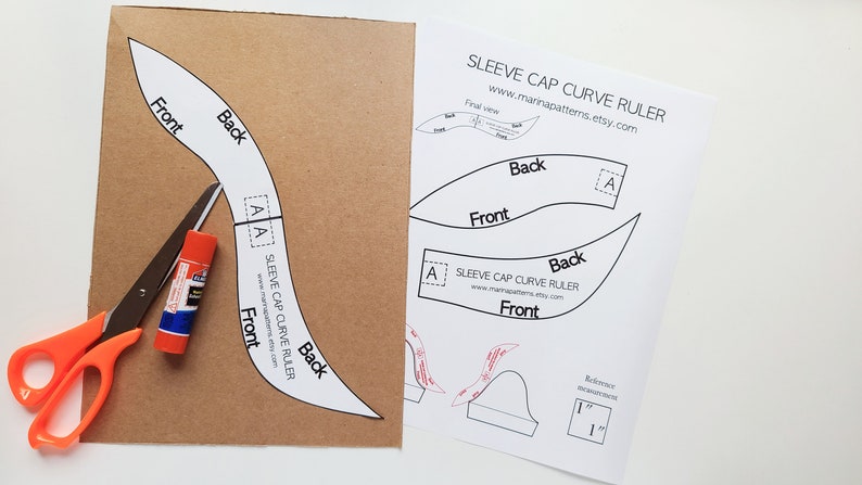 May include: A sewing pattern for a sleeve cap curve ruler is shown with scissors and glue stick. The pattern is printed on cardboard and paper, with the words "Front" and "Back" labeled on the pattern pieces. The scissors have orange handles.
