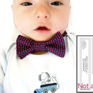 May include: A baby wearing a white shirt with a red and blue bow tie with white stars. The bow tie is not adjustable. The shirt has a small embroidered design of a dog on a toy car.