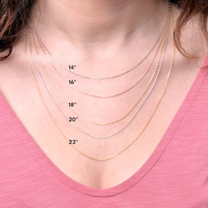 May include: A close-up of a woman's neck wearing five different chain necklaces in gold, silver, and rose gold. The necklaces are labeled with their lengths: 14", 16", 18", 20", and 22".