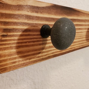 May include: A wooden wall-mounted coat rack with three round, gray stone knobs. The wood has a natural, rustic finish.