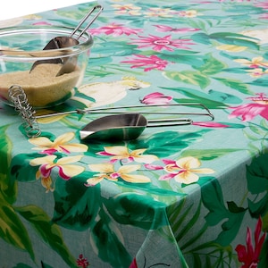 May include: A turquoise tablecloth with a vibrant floral pattern featuring pink, yellow, and white flowers, and green leaves. A clear glass bowl filled with brown sugar and metal scoops sits on the tablecloth. A metal whisk is also visible.