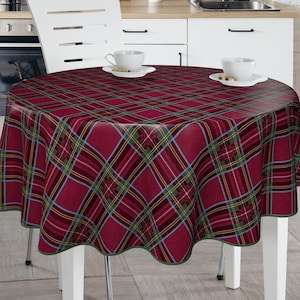 May include: Red and green plaid tablecloth with a scalloped edge. The tablecloth is laid on a round table with two white cups and saucers on the table.