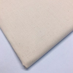May include: A close-up of a piece of off-white fabric with a slightly textured surface. The fabric has a subtle speckled pattern.