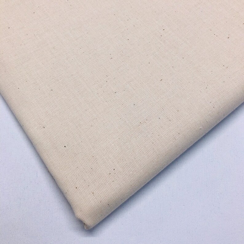 May include: A close-up of a piece of off-white fabric with a slightly textured surface. The fabric has a subtle speckled pattern.