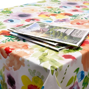 Peut inclure: Une nappe blanche avec un imprim&eacute; floral aquarelle dans des tons de rose, jaune, bleu, vert et orange. La nappe a une pile de magazines dessus.