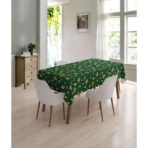 May include: A green tablecloth with a gingerbread man pattern. The tablecloth is on a wooden table with two white chairs.