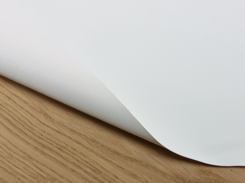 Puede incluir: Primer plano de una tela de lona blanca con un ligero pliegue, mostrando la textura del material. La tela est&aacute; sobre una superficie de madera marr&oacute;n claro.