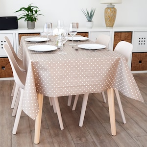 May include: A dining table set for four, with a tan tablecloth adorned with white polka dots. The table is surrounded by four light-colored chairs. White plates, glasses, and cutlery are set. The table is approximately 122 cm long.