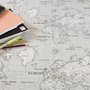 May include: A world map printed in black and white on a light gray background. A calculator, a stack of notebooks, and pencils are on top of the map.