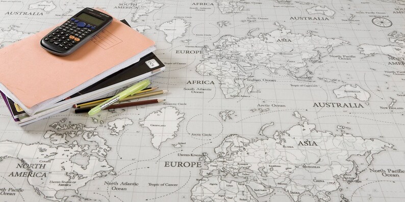 May include: A world map printed in black and white on a light gray background. A calculator, a stack of notebooks, and pencils are on top of the map.