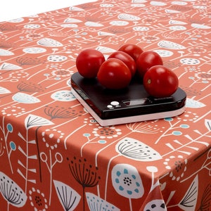 May include: A red tablecloth with a white floral pattern. Five red tomatoes are on a black digital kitchen scale on the tablecloth.