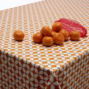 May include: A brown tablecloth with a white geometric pattern featuring small orange mandarins on top.